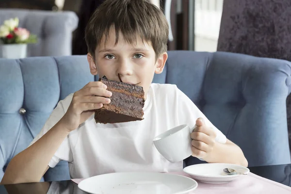 O menino está comendo uma grande fatia de bolo — Fotografia de Stock