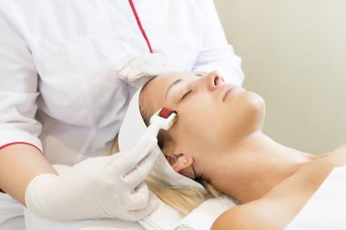 The woman undergoes the procedure of medical micro needle therapy with a modern medical instrument derma roller. clipart