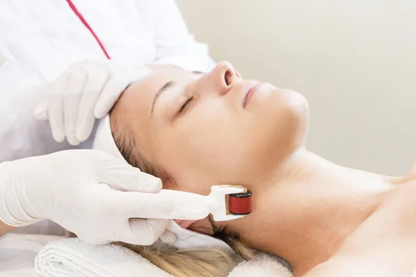 The woman undergoes the procedure of medical micro needle therapy with a modern medical instrument derma roller.
