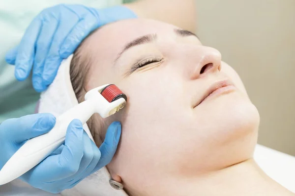 The woman undergoes the procedure of medical micro needle therapy with a modern medical instrument derma roller