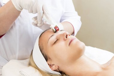 The woman undergoes the procedure of medical micro needle therapy with a modern medical instrument derma roller  clipart