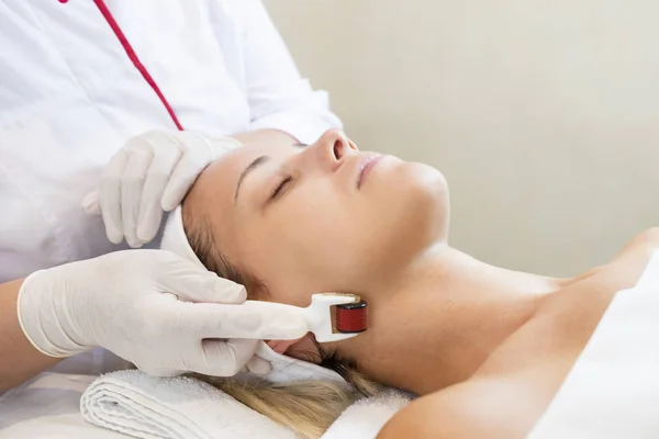 The woman undergoes the procedure of medical micro needle therapy with a modern medical instrument derma roller