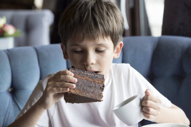 Oğlan elinde büyük bir dilim pasta yiyor 