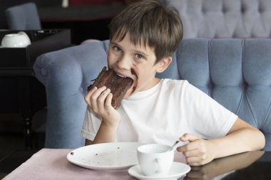Oğlan elinde büyük bir dilim pasta yiyor 
