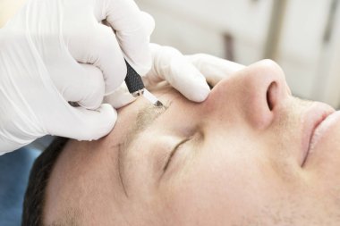 Bir adamın kaşlarını güzellik salonunda iyileştirmek için genç bir adamın mikropatinaj prosedürü..