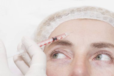 Orta yaşlı bir kadının karşısında güzellik salonunda kozmetik enjeksiyon prosedürü..