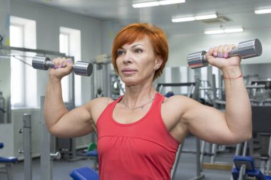 Yaşlı bir kadın spor salonunda beden eğitimi dersi alıyor..