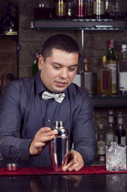 Barda barmenlik yapan genç bir adam müşterilere içki hazırlıyor..