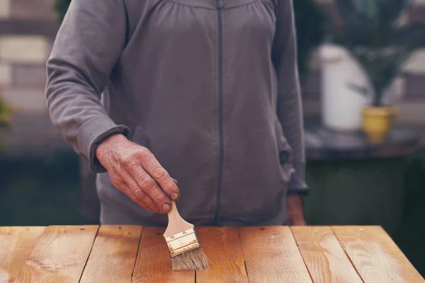 Hand einer Seniorin beim Bemalen eines Holztisches — Stockfoto