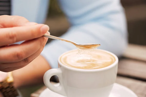 Cuchara en una mano femenina vertiendo azúcar en su taza de café — Foto de Stock