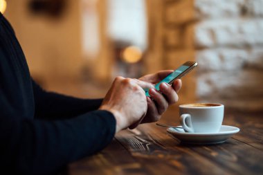 Adam kafedeki cep telefonunu kullanarak internet bankacılığına giriyor.