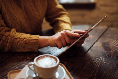 Kadın kafedeki masada tablet kullanıyor.