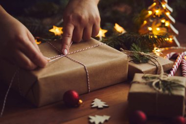 Masanın üzerinde Noel hediyesi paketleyen bir kadın.