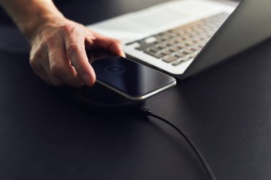 Adam masadaki kablosuz şarj cihazına cep telefonu yüklüyor.