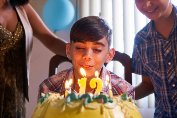 День рождения с счастливым латиноамериканским мальчиком, дующим свечами на торт — стоковое фото