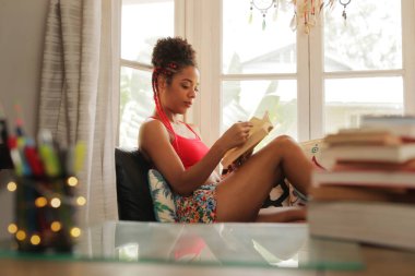 Afrikalı-Amerikalı kadın okuma kitabı evde pencere yakınındaki