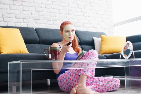 Chica con máscara de belleza leyendo y viendo la televisión en casa — Foto de Stock