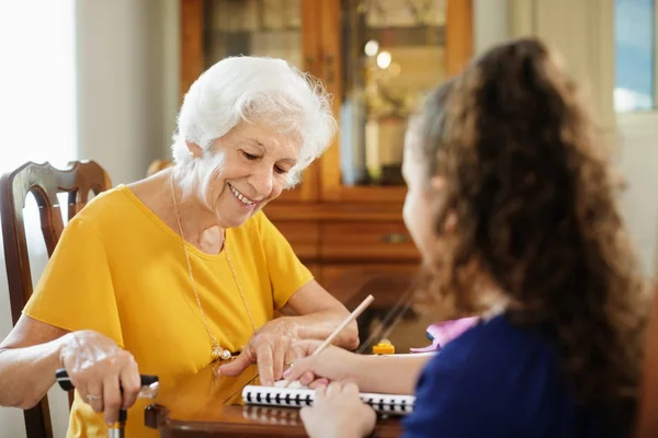 Bejaarde vrouw helpen weinig meisje doen School huiswerk — Stockfoto