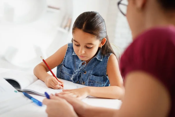 Hispanic Mother Helping Girl Doing School Homework At Home