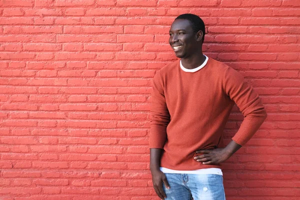 Afrikanischer junger Mann lächelt und lehnt an roter Wand — Stockfoto