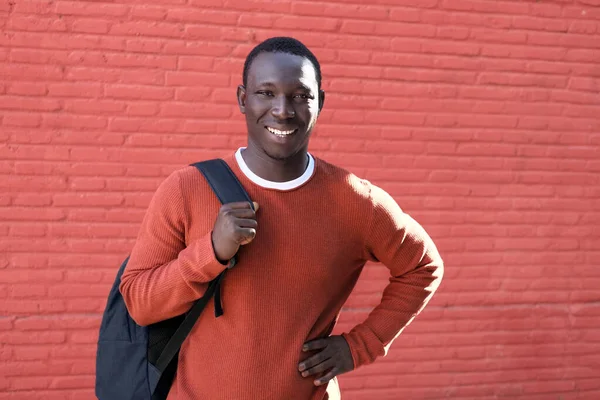 Jovem africano sorrindo e segurando mochila na parede vermelha — Fotografia de Stock