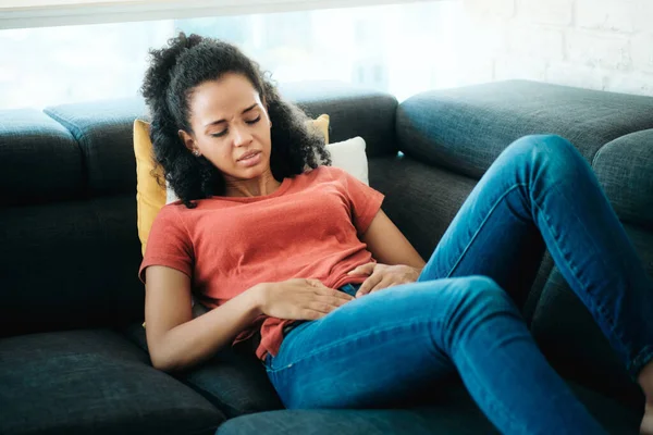 Young Black Woman With Menstrual Pain Lying On Sofa — Stok fotoğraf
