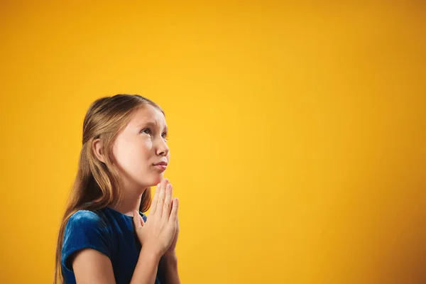 Portrait de petite fille caucasienne priant Dieu sur fond jaune — Photo