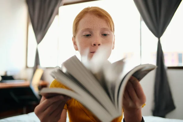 Młoda ruda dziewczyna studiuje i patrząc przez książkę — Zdjęcie stockowe