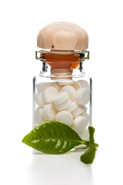 Білі таблетки в скляній тарі з дерев'яним верхом і зеленим листом — стокове фото