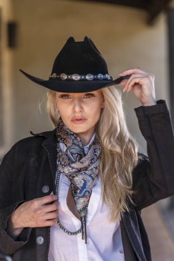 Kovboy gibi giyinmiş muhteşem sarışın bir manken. Açık havanın tadını çıkarıyor.