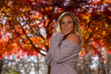 Muhteşem sarışın bir model parkta sonbahar gününün tadını çıkarıyor.