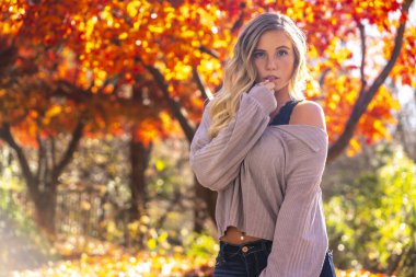 Muhteşem sarışın bir model parkta sonbahar gününün tadını çıkarıyor.