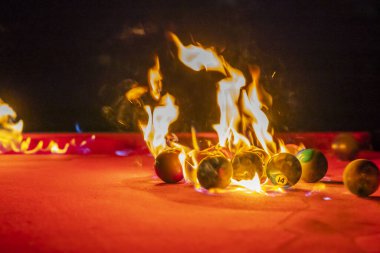 Açık bir ortamda dışarıda otururken bilardo topları ateşte fotoğraflanır.