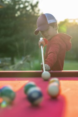 Küçük bir çocuk açık havada bilardo oynuyor.