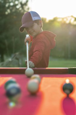 Küçük bir çocuk açık havada bilardo oynuyor.