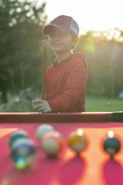 Küçük bir çocuk açık havada bilardo oynuyor.