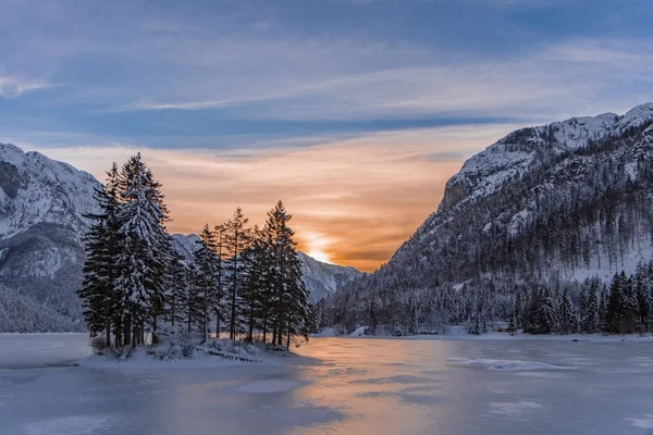 Isla con árboles en invierno lago congelado Predil y puesta de sol — Foto de Stock