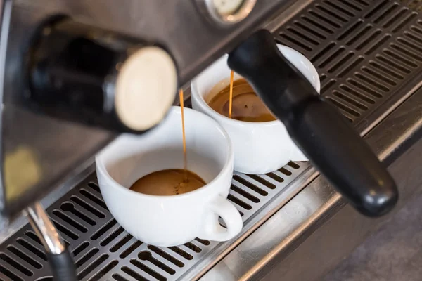 Espresso dripping from portafilter of coffee machine into white cup
