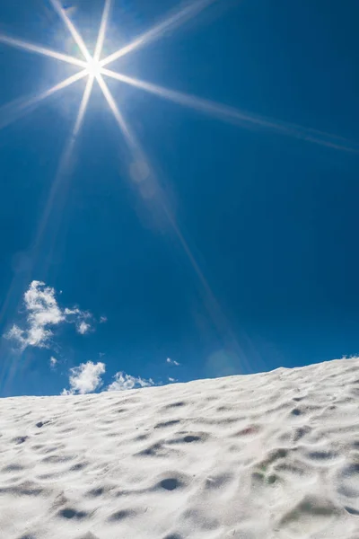 Snowy mountain with sun flares on blue sky with clouds