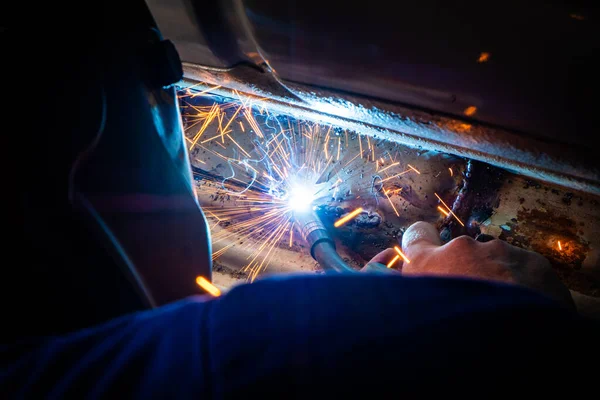 Man welds in metal of car and repairs rusty hole — Stock Photo, Image