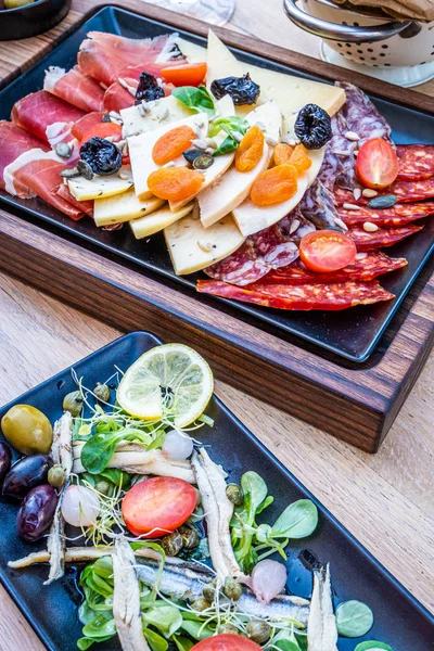 Antipasti on wooden plate, salad with anchovy, bread on paper — 스톡 사진