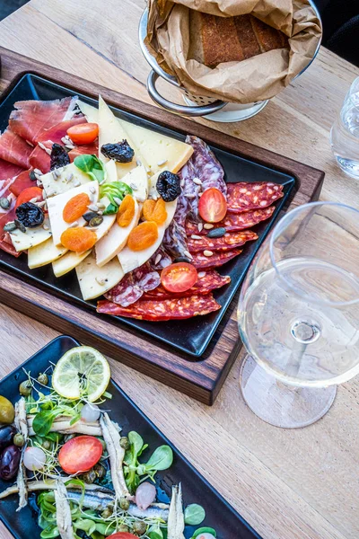 Antipasti on wooden plate, salad with anchovy, bread on paper — 스톡 사진