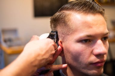 Berber, berber dükkanında ustura olan genç bir adamın saçını kesiyor.