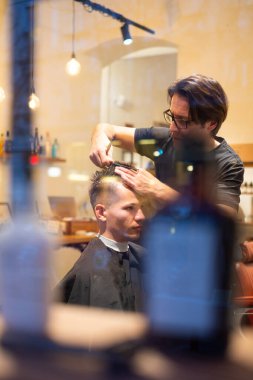 Berber, genç bir adamın saçını makas ve berber dükkanında tarak ile keser.