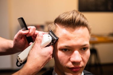 Berber, berber dükkanında ustura olan genç bir adamın saçını kesiyor.