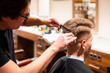 Berber, genç bir adamın saçını makas ve berber dükkanında tarak ile keser.