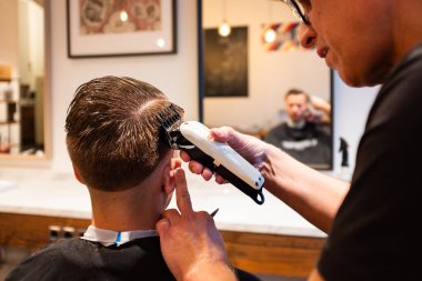 Berber, berber dükkanında ustura olan genç bir adamın saçını kesiyor.