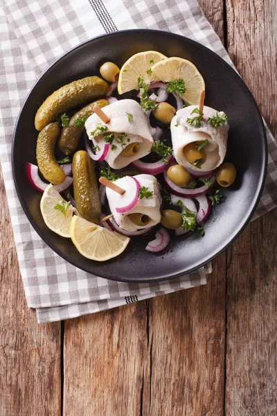 rolls of marinated herring with olives, onions, pickles and lemo