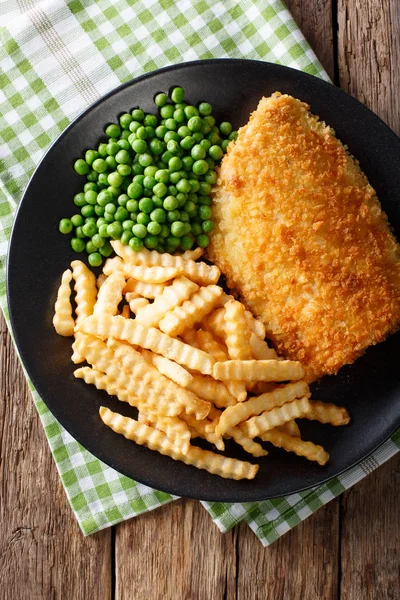 Рыба и чипсы с зеленым горохом крупным планом на тарелке. Вертикальный верх — стоковое фото