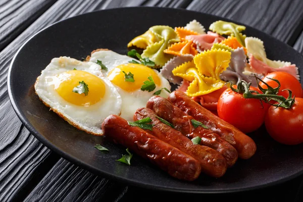 Fried eggs with sausages, colored farfalle pasta and tomatoes cl — Stock Photo, Image